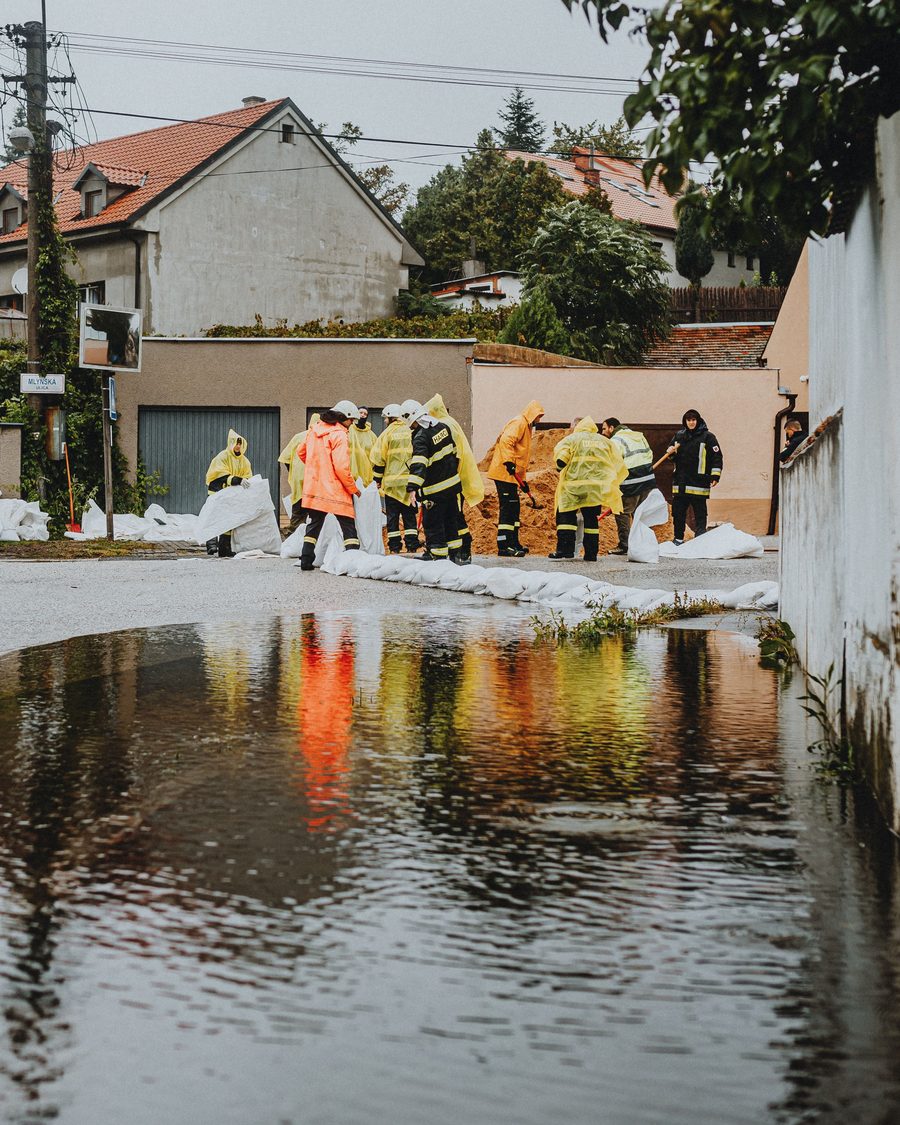Rue de lotissement inondée après un orage, pompiers et sacs de sable devant un garage